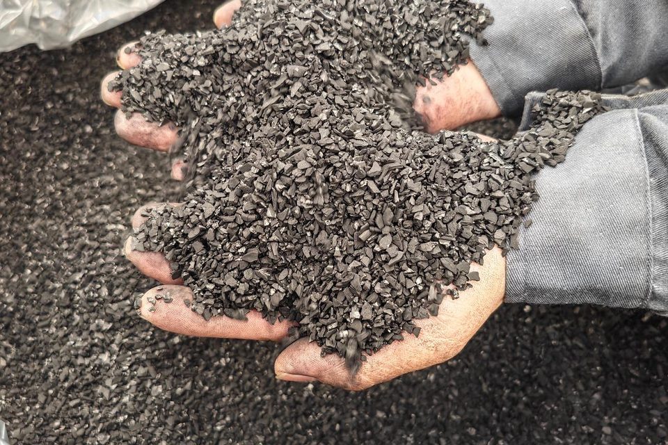 Hands holding activated carbon granules above an open lined bag