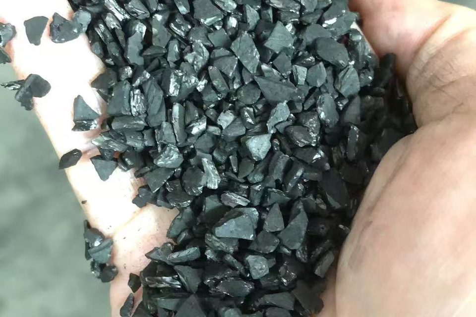 Close-up of irregular black activated carbon granules in a hand